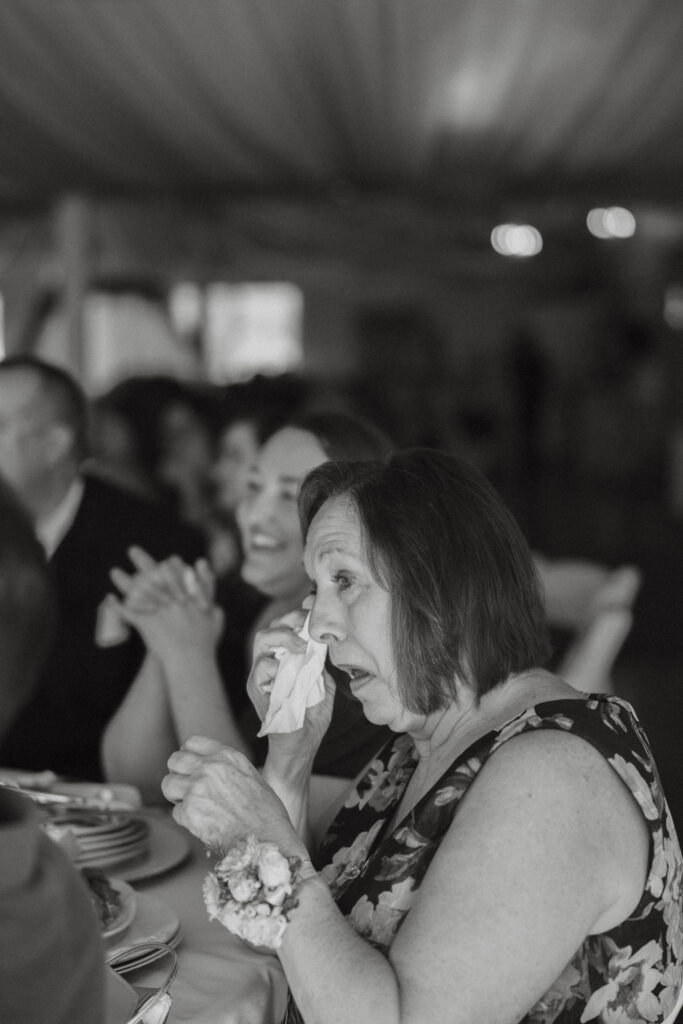 Candid black-and-white photo of an emotional grandma wiping away tears during reception speeches at a large wedding in Wisconsin, by Alex McCrary Photography.