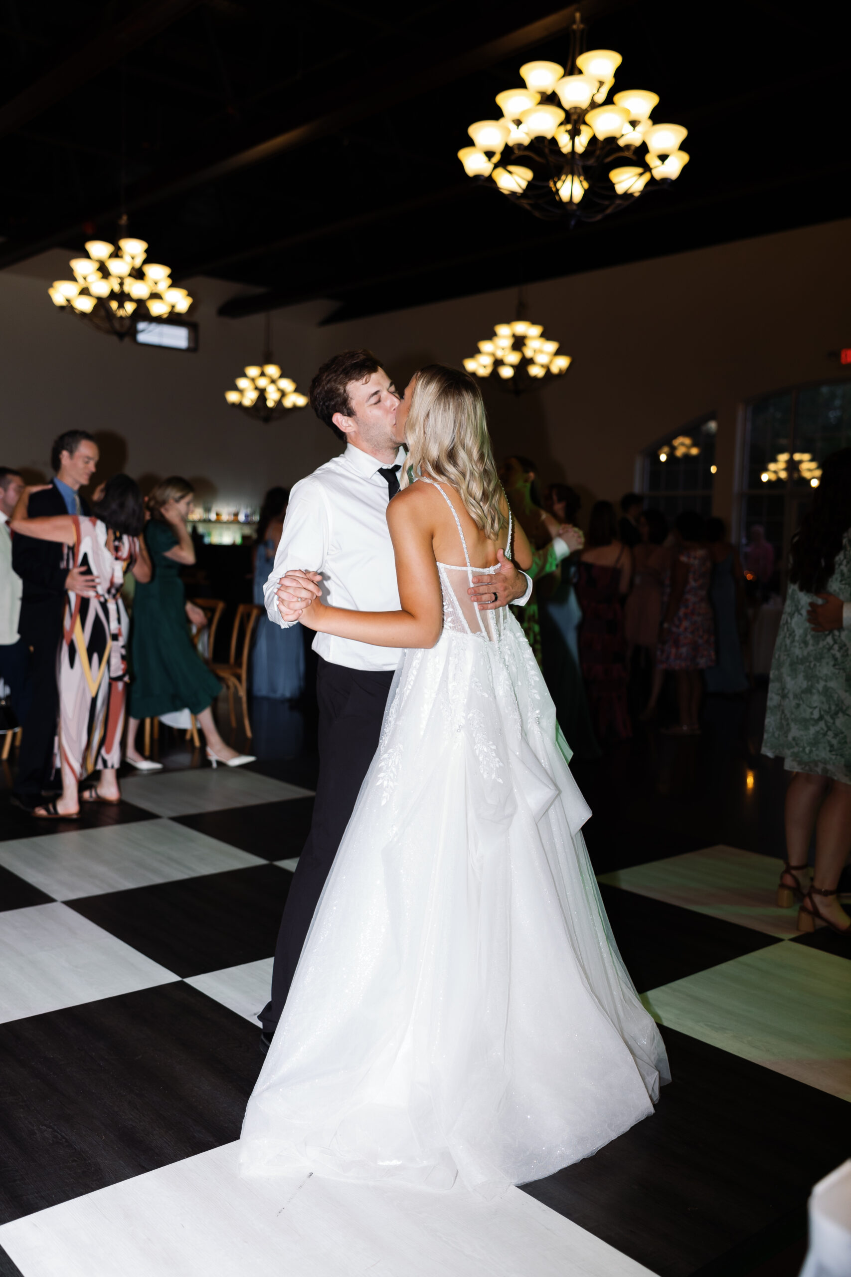 bride and groom dancing on checkered dance floor during their wedding reception with guests in the background